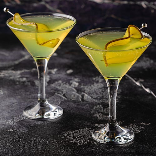 Two Martini glasses on a dark background with pickle garnishes