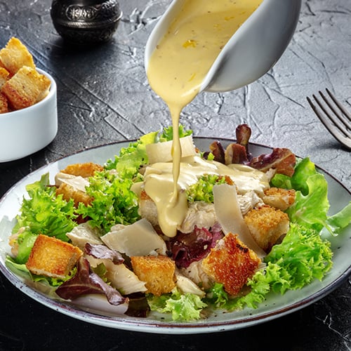 salad dressing in a sauce cup being poured over a green salad