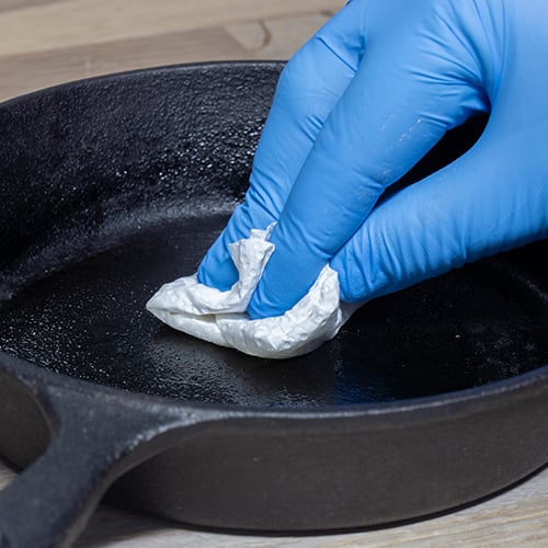close up of a hand wiping down a cast iron pan