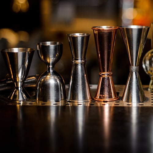 Five jiggers of different sizes lined up on a table