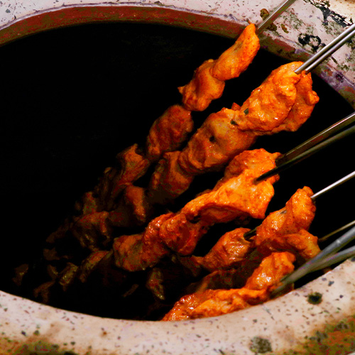 Close up of chicken on sticks sitting in a large cooking vessel