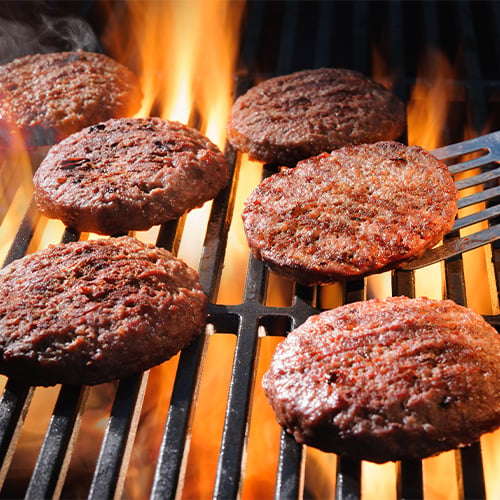 Grouping of burgers on a grill with a spatula flipping one 