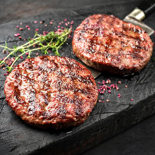 two burgers on a stone surface with grill marks and herbs