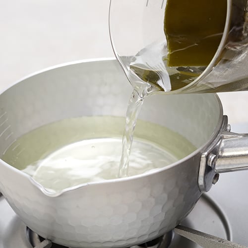 A cup pouring broth in to a sauce pan