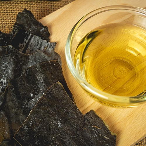Sheets of seaweed and a cup of broth on a cutting board