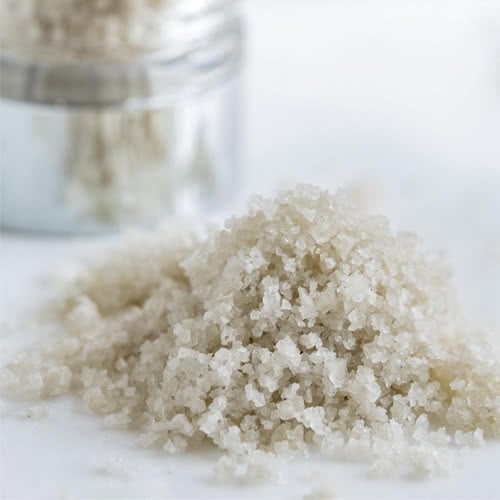 Gray Celtic salt in a pile on marble surface with glass jar in background