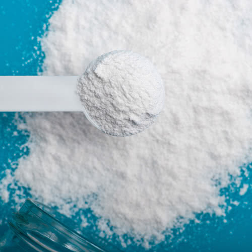 White powder salt in a pile on a blue surface with white spoon holding salt on top