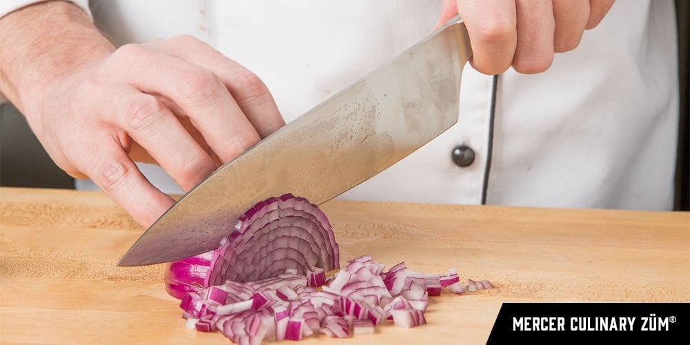 A chef using a Mercer Culinary ZüM® to cut a red onion