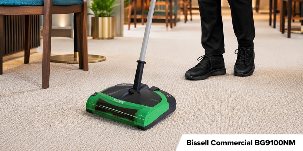 Bissell Commercial BG9100NM - Person using a compact green-and-black Bissell commercial carpet sweeper on light-colored restaurant carpeting.