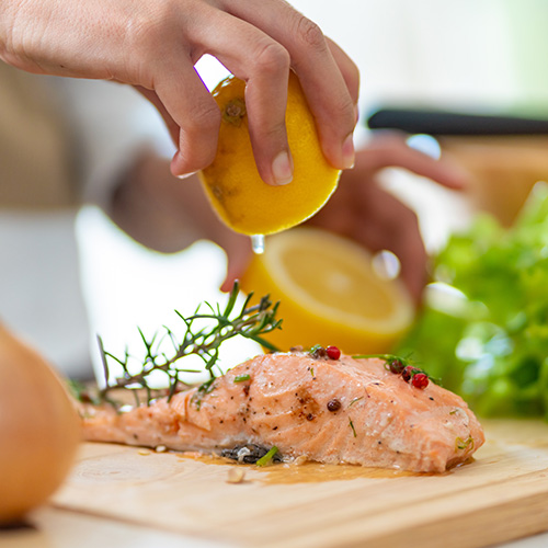 Close up of Asian woman hand squeeze lemon juice on piece of salmon steak