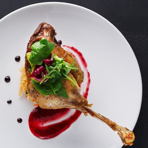 Duck confit with vegetables on black background