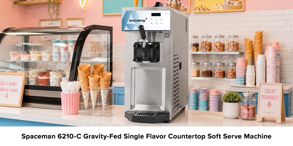Spaceman 6210-C countertop soft serve machine in a colorful ice cream shop with cones, cups, toppings, and a refrigerated display case.