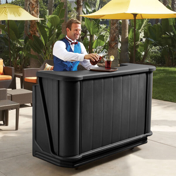 A man standing behind a black Cambro portable bar with a drink.
