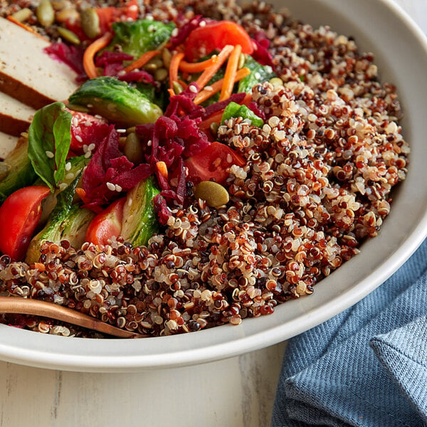 A bowl of Organic Tri-Color Quinoa salad on a table with a blue cloth.