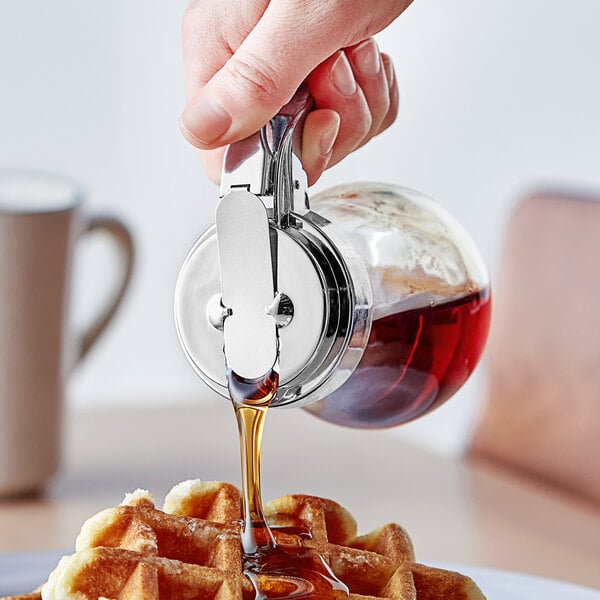 A person pouring syrup on a waffle using an American Metalcraft syrup dispenser.