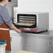 A woman wearing an apron putting cookies in an Avantco countertop convection oven.