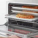 A person opening an Avantco countertop convection oven with a pizza inside.