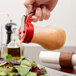 A hand pouring syrup from a red Tablecraft syrup dispenser over a salad.