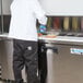 An Avantco 2 door refrigerated sandwich prep table with a person in a white coat and blue gloves preparing a sandwich.