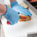 A person in blue gloves making a sandwich on an Avantco refrigerated prep table.