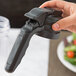A hand using a Tablecraft polypropylene dispenser top on a black container on a kitchen counter.