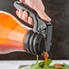 A hand using a Tablecraft sauce dispenser to pour liquid into a container.