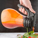 A hand pouring tomato sauce from a Tablecraft Tritan dispenser into a bowl of salad.