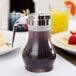 A Tablecraft syrup dispenser filled with syrup on a table next to a plate of pancakes.